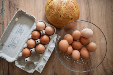 Karton ve cam kasede taze kahverengi yumurtalar. Ahşap mutfak masasında taze çiftlik yumurtaları.