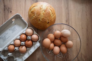 Karton ve cam kasede taze kahverengi yumurtalar. Ahşap mutfak masasında taze çiftlik yumurtaları.