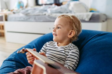 Küçük çocuk evde gitar çalmaya çalışıyor, eğleniyor..