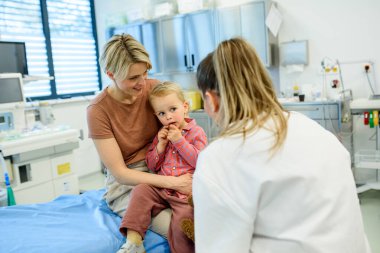 Kadın çocuk doktoru, önleyici sağlık kontrolü sırasında küçük çocukla konuşuyor..