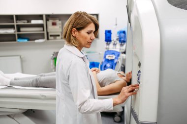 Bayan doktor CT makinesini çalıştırıyor ve hastayı taramaya hazırlıyor.