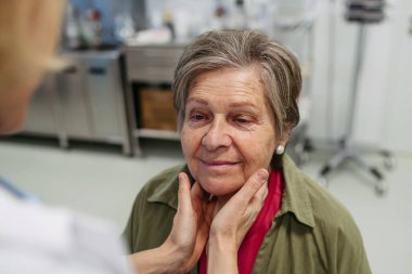 Yaşlı kadın hastaların tıbbi muayenesi sırasında lenf düğümlerini elle muayene eden doktor.