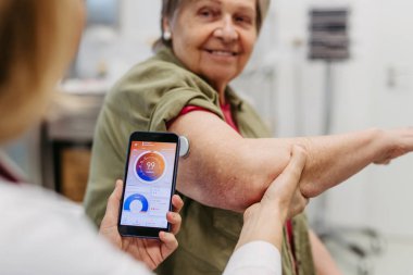 Endokrinolog, yaşlı hastaya sürekli glikoz monitörünü mobil uygulamayla nasıl bağlayacağını öğretiyor. Kıdemli sağlık hizmetleri.