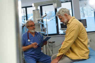 Muayene masasındaki hasta üzgün, doktora sağlık sorunları ve semptomları anlatıyor..