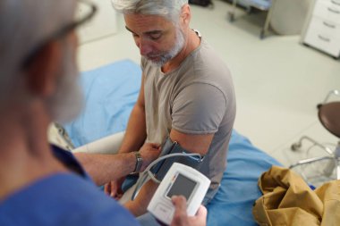 Doktor hastaların tansiyonunu dijital tansiyon monitörü kullanarak ölçüyor..