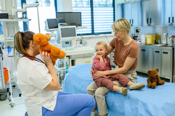 Kadın çocuk doktoru kontrol sırasında oyuncak ayıyla küçük çocuğu rahatlatıyor.