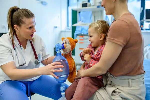 Kadın çocuk doktoru, genç hastaya oyuncak ayının üzerinde oksijen maskesi göstermiş.