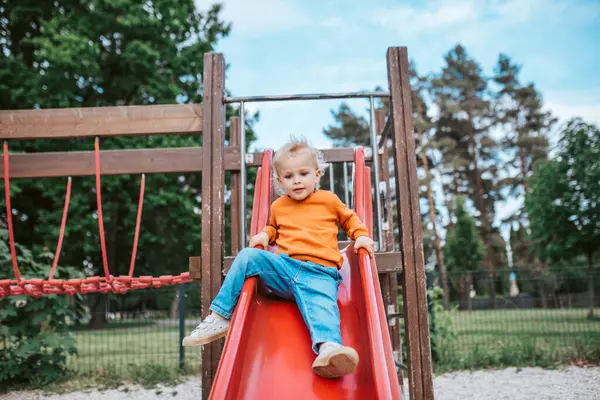 Küçük çocuk kaymaya hazırlanıyor. Çocuk oyun alanında eğleniyor..