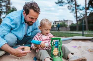 Baba ve küçük çocuk oyun parkında oynuyorlar, hafta sonu eğlencesi..
