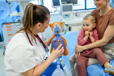 Kadın çocuk doktoru, genç hastaya oyuncak ayının üzerinde oksijen maskesi göstermiş.