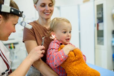 Otolaryngolog, yürümeye yeni başlayan çocuğu pediatri kliniğinde muayene ediyor..