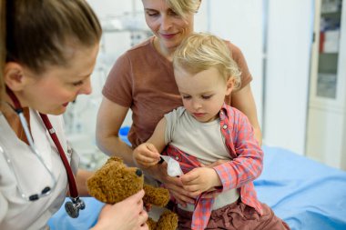 Doktor ve genç bebek hasta sağlık kontrolü sırasında oyuncak ayıyı tedavi ediyor..