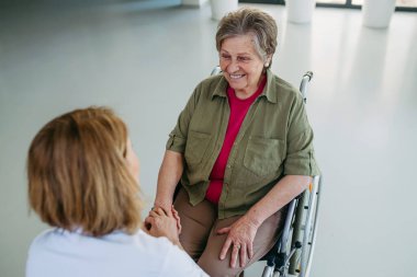 Hademeyle konuşurken tekerlekli sandalyedeki yaşlı kadın gülümsüyor..