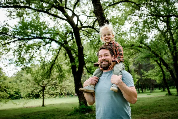 Babam parkta yürürken gülümseyen oğlunu omuzlarında taşır.