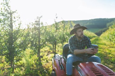Meyve bahçesinde küçük bir traktör üzerinde oturan olgun çiftçi, huzurlu anın tadını çıkarıyor..
