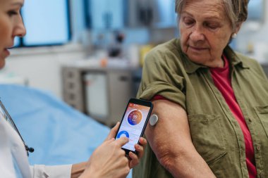 Endokrinolog, yaşlı hastaya sürekli glikoz monitörünü mobil uygulamayla nasıl bağlayacağını öğretiyor. Kıdemli sağlık hizmetleri.