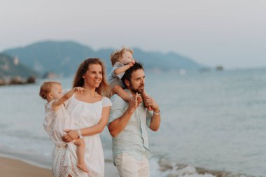 Küçük çocuklu ebeveynler deniz kenarında yaz akşamının tadını çıkarıyor, gün batımını izliyorlar..