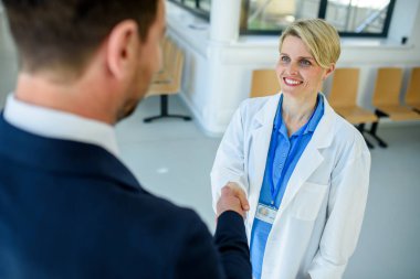 Doktor ilaç temsilcisiyle görüşüyor ve klinik ortamda elini sıkıyor..