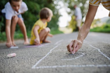 Anne ve çocuklar sıcak yaz günlerinde yolda tebeşirle çizim yapıyorlar..