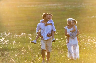 Genç bir aile, yeşil yaz akşamında çimlerin üzerinde oturarak huzurlu bir yaz akşamının tadını çıkarıyor..