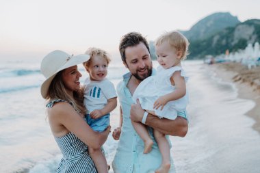 Küçük çocuklu ebeveynler deniz kenarında yaz akşamının tadını çıkarıyor, gün batımını izliyorlar..