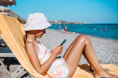 Gril, elinde akıllı telefonuyla plaj şezlongunda dinleniyor. Yaz tatili.