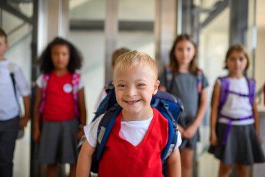 Okul koridorunda dikilen üniformalı çocuklar arasında Down sendromlu bir çocuk. Okul konseptine dönelim..