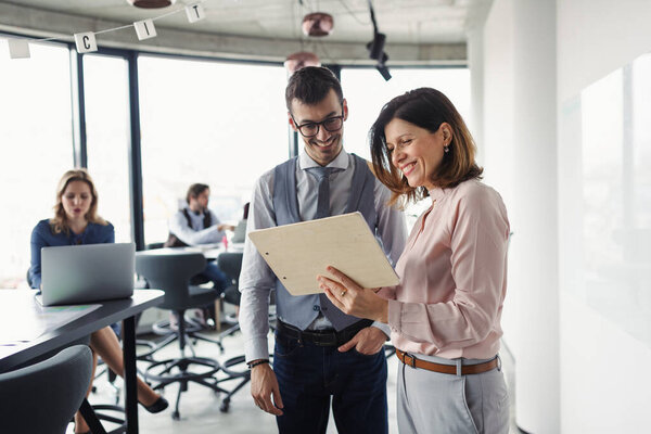 Male and female collegues talking about project document, standing in modern office.