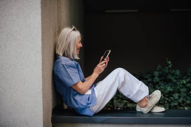 Yaşlı hemşire hastane vardiyasında dinleniyor, dışarıda mola veriyor. Yan görünüm.