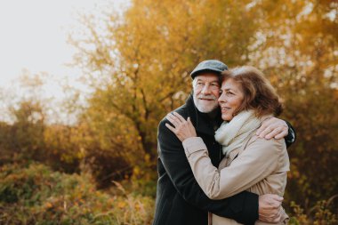 Sonbahar yapraklarıyla çevrili yaşlı bir çift tarafından sonbahar ormanlarında romantik bir yürüyüş..