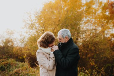 Sonbahar yapraklarıyla çevrili yaşlı bir çift tarafından sonbahar ormanlarında romantik bir yürüyüş..
