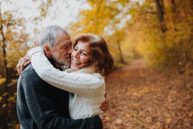 Yaşlı çift sonbahar mevsiminde, sonbahar yapraklarıyla çevrili olarak dışarıda vakit geçiriyorlar..