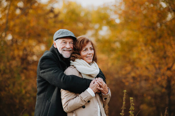 Older couple spending time outdoors in fall season, surrounded by autumn leaves.