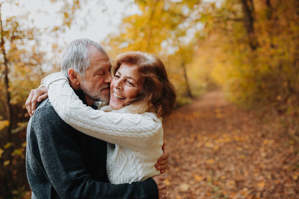 Старшая пара проводит время на свежем воздухе осенью, в окружении осенних листьев.