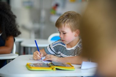 Okullu çocuk sınıftaki masada oturuyor, not alıyor..