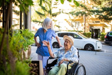 Tekerlekli sandalyedeki yaşlı kadına yardım eden kadın hemşire, vitrine bakıyor..