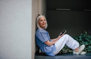 Yaşlı hemşire hastane vardiyasında dinleniyor, dışarıda mola veriyor. Yan görünüm.