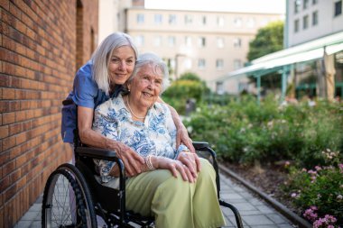 Tekerlekli sandalyedeki yaşlı kadın, bakıcı asistanıyla temiz havanın tadını çıkarıyor..