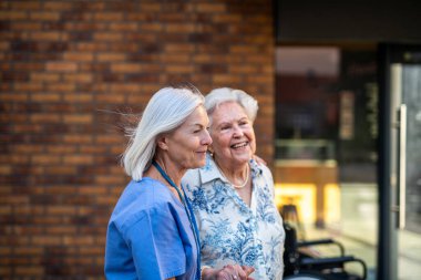 Ev bakıcısı yaşlı hastayı şehirde yürüyüşe çıkarıyor..