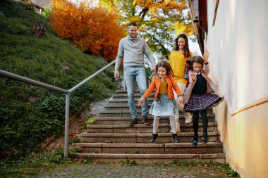 Kız kardeşler ve ebeveynler sıcak bir sonbahar gününde parkın merdivenlerinden aşağı iniyorlar. Hindistan yaz konsepti.