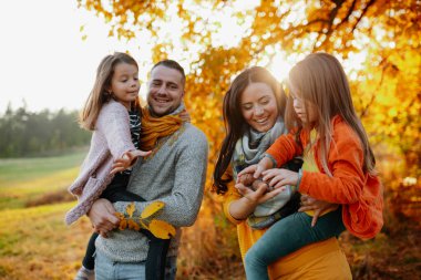 Günbatımında sonbahar doğada bir zeminde oturan iki küçük çocuklu mutlu genç aile portresi.