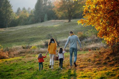 Sonbahar doğasında gün batımında iki küçük kızı olan ailenin arka görüntüsü..