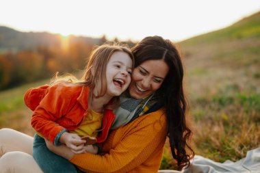 Sonbahar doğada bir zemin üzerinde oturan küçük bir kızı ile genç anne portresi.