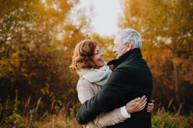 Sonbahar yapraklarıyla çevrili yaşlı bir çift tarafından sonbahar ormanlarında romantik bir yürüyüş..