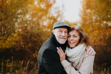 Yaşlı çift sonbahar mevsiminde, sonbahar yapraklarıyla çevrili olarak dışarıda vakit geçiriyorlar..