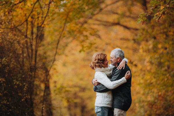 Older couple spending time outdoors in fall season, surrounded by autumn leaves.