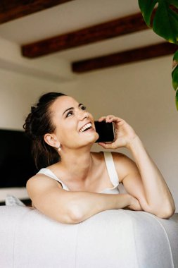 Kendine güveni tam bir kadın koltukta oturuyor ve evde huzurlu bir şekilde telefonla konuşuyor..