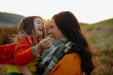 Sonbahar doğada bir zemin üzerinde oturan küçük bir kızı ile genç anne portresi.