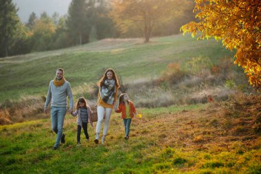 Günbatımında sonbahar doğada bir zeminde oturan iki küçük çocuklu mutlu genç aile portresi.