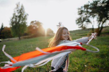 Sonbahar doğasında gün batımında gökkuşağı eli uçurtmasıyla oynayan mutlu küçük kız..